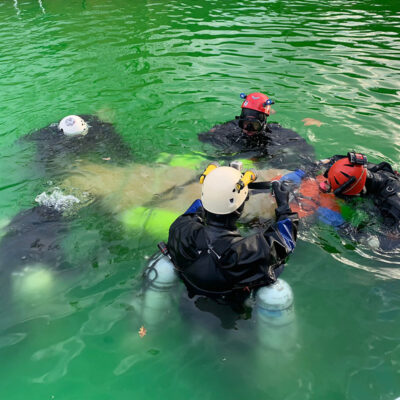 Divers practicing the appropriate packaging of a casualty into a stretcher for an underwater dive rescue.