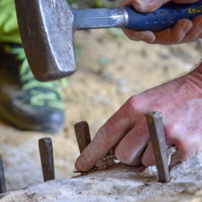 Rock splitting with plug and feathers inserted into chain drilled pilot holes.